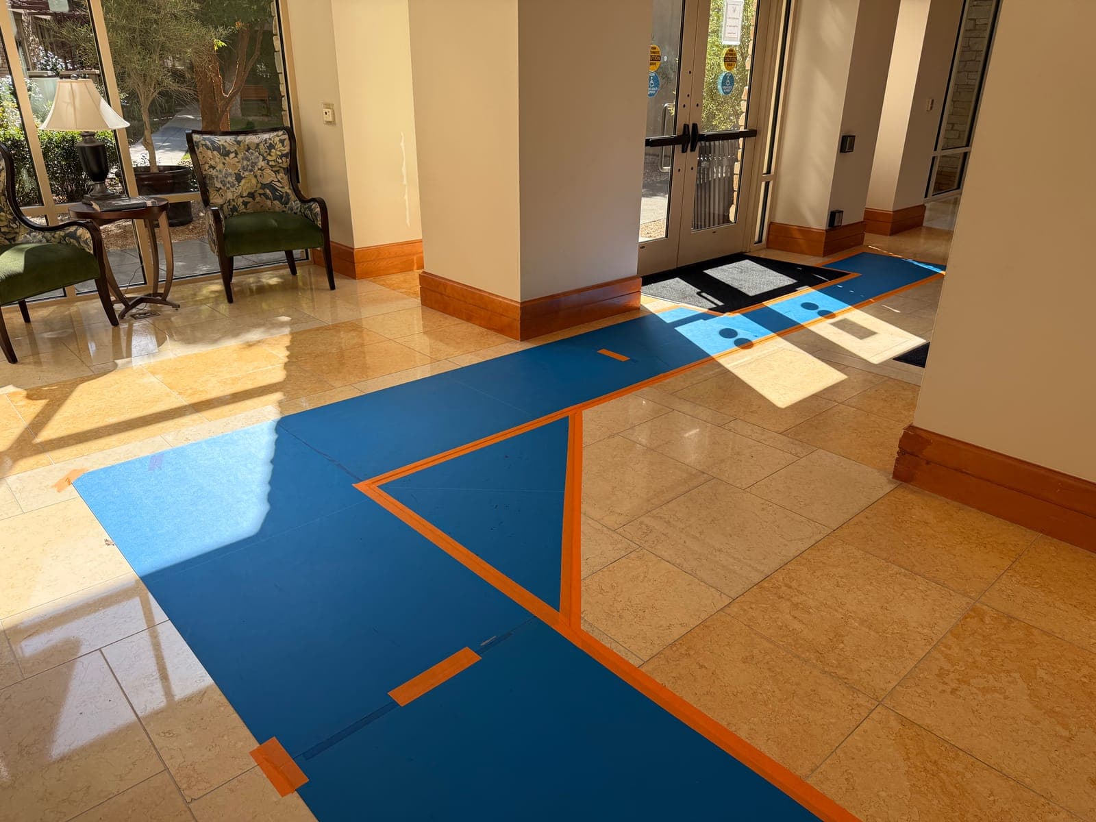 A protected blue floor route taped across a polished stone lobby, running from the entrance doors into the building