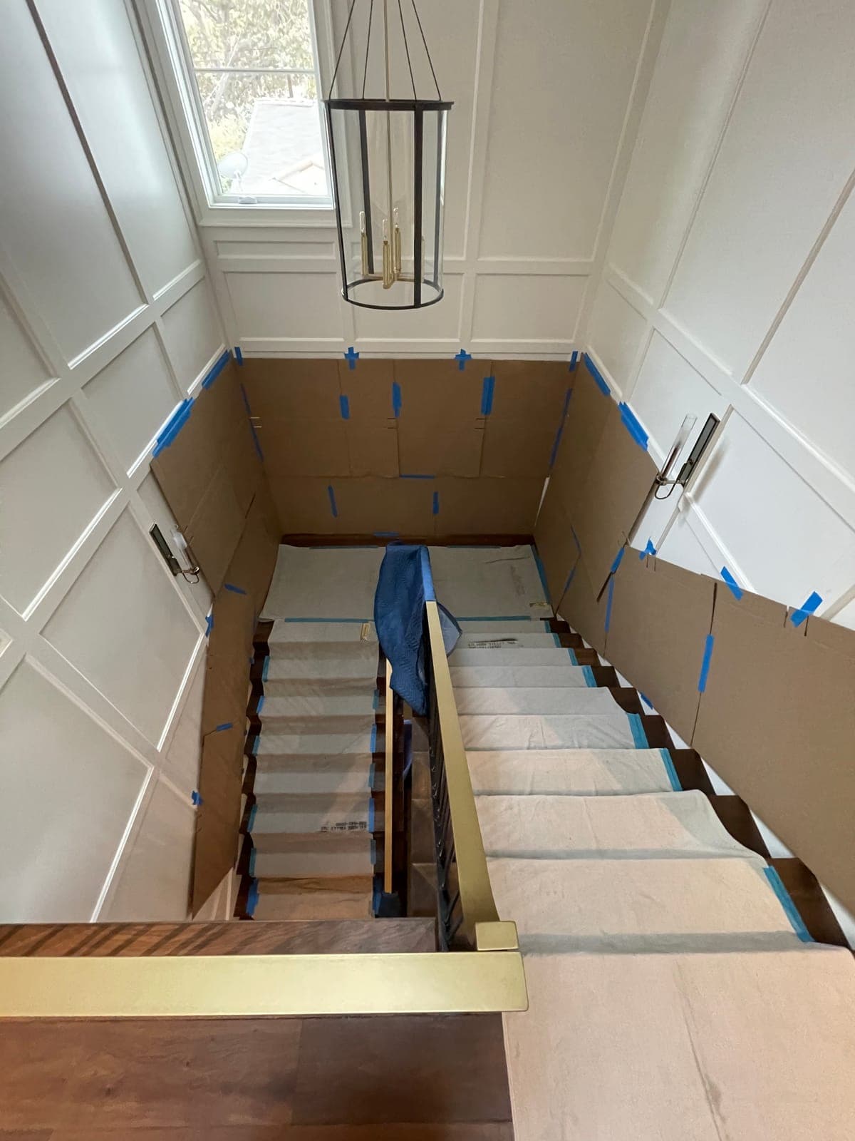 A staircase and hallway fully protected with cardboard on the walls, padded rails and covered treads before a move