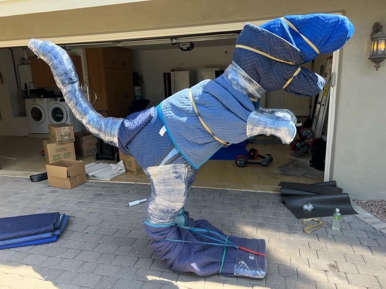A large oversized item fully wrapped in moving blankets and shrink, banded and standing on a driveway